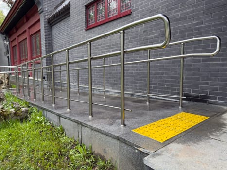 Stainless steel accessibility ramp with bright yellow tactile paving for visually impaired individuals, located next to building, highlighting inclusive design and care for people with disabilities