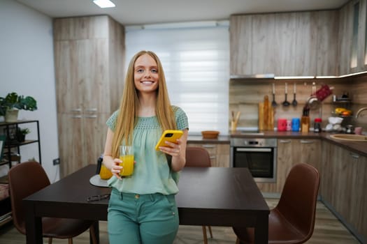 Bright and cheerful woman holds a drink and phone in a stylish kitchen.