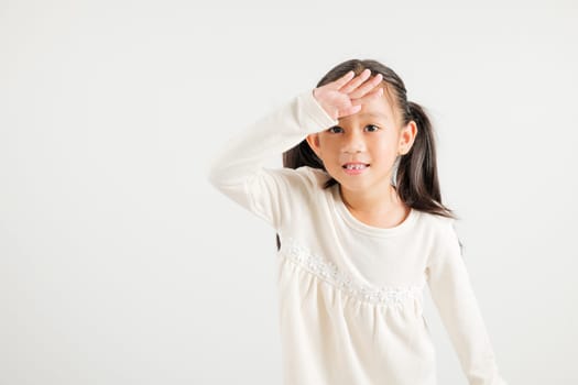 Searching concept. Asian young girl kid looking far away with hand over head at studio shot isolated on white background, Portrait of Happy kindergarten child looking at distance with eyes shaded