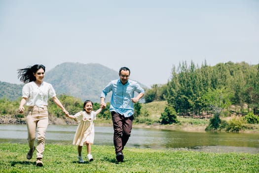 Asian family father mother and daughter holding hands and running lake in park, lifestyle parents and child kid enjoying outdoors together in nature on summer travel, Family relaxation, Front view