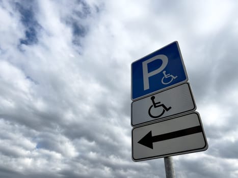 Handicap parking sign with directional arrow on cloudy day, indicating accessible parking for people with disabilities, promoting inclusion and barrier free infrastructure