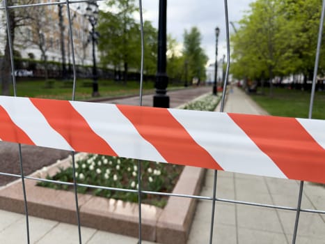 Warning tape on metal fence blocks access to landscaped park area during maintenance, symbolizing safety, restricted entry, and temporary closure for improvement works
