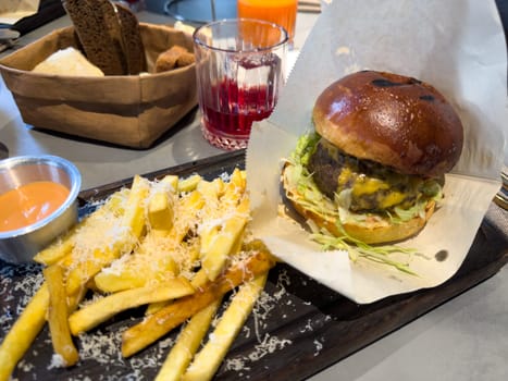 Juicy cheeseburger with fresh lettuce served on a toasted bun, accompanied by golden fries topped with grated cheese and creamy sauce. Cozy dining atmosphere with drinks and food