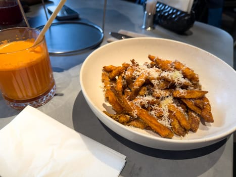 Bowl of sweet potato fries sprinkled with grated cheese served alongside a glass of fresh carrot juice. Healthy snack choice in cozy cafe, ideal for balanced and nutritious eating