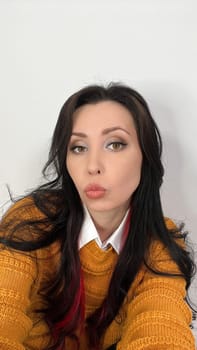 Close-up of a beautiful brunette woman with long hair, wearing a yellow sweater and white collar shirt, playfully pouting her lips. Ideal for fashion and lifestyle themes.