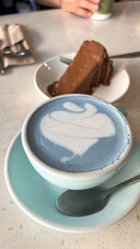 Indulge in a beautiful blue latte artfully presented next to a decadent slice of rich chocolate cheesecake. A perfect pairing for a cozy cafe atmosphere, ideal for social media or food blogs.