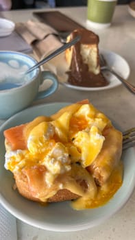 A beautifully plated Eggs Benedict with poached eggs, smoked salmon, and rich hollandaise sauce. Served with a decadent chocolate cheesecake, perfect for brunch or dessert lovers.
