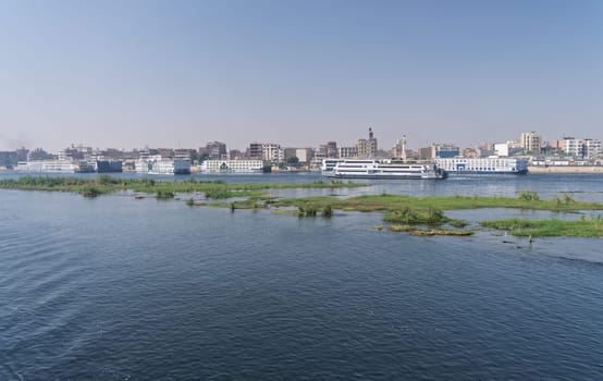 Crowded harbor in Edfu with Nile cruise boats docked and others leaving for Aswan on river in Egypt
