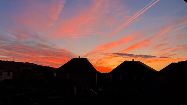 A stunning sunset illuminates the sky with shades of orange and pink over suburban rooftops. Vapor trails create accents across this serene urban landscape, offering a picturesque view.