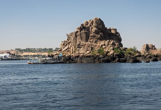 Tourists in ferry boat passing rocky island on way to Philae Temple in Aswan reservoir