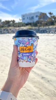 Miami, FL USA - February 05, 2025: Hand holding cup of hot McCafe drink. The ocean waves and a building create a perfect backdrop for a leisurely moment by the coast, ideal for travel and enjoyment.