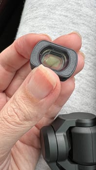 Close-up of a hand holding a small scratched camera lens, highlighting precision optics and technology. Perfect for themes in photography, videography, and modern advancements in creative projects.