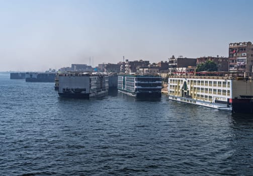 Crowded harbor in Edfu with Nile cruise boats docked and others leaving for Aswan on river in Egypt