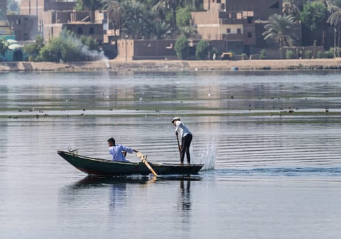 Luxor, Egypt - 1 November 2024: Two men in their small boat on a calm river Nile while tending to fishing net in the water
