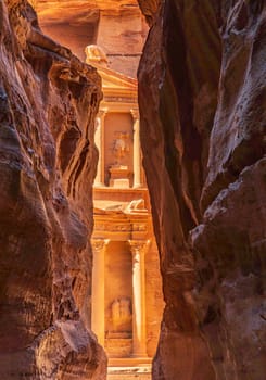 The carved facade of the Treasury building or Al-Khazneh in the ancient city of Petra in Jordan seen through narrow Siq gorge