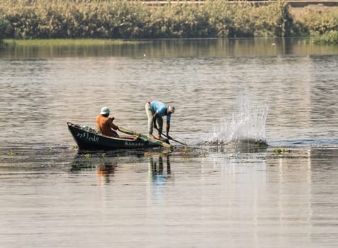 Luxor, Egypt - 1 November 2024: Two men in their small boat on a calm river Nile while tending to fishing net in the water
