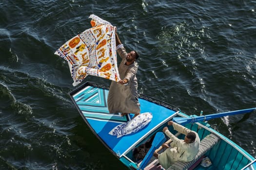Esna, Egypt - 6 November 2024: Nile River on a sunny day featuring a vendor in a small rowboat selling textiles to a cruise ship