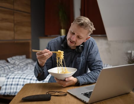 Asian Man Eating Noodles In Front Of A Laptop In Bedroom