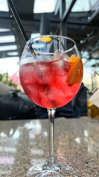 A close-up of a refreshing red cocktail with ice cubes and an orange slice in a wine glass on a bar counter, creating a vibrant summer drink experience. Perfect for menus and promotions.