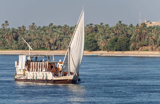 Dahabiya Nile cruise ship sailing alongside a sandy desert with palm trees on the River Nile near Aswan