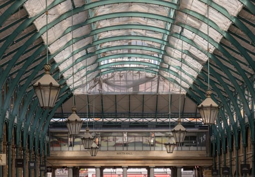 London, UK - May 13, 2025 - Architecture greco-roman style with iron glass roof and Lanterns hanging on the ceiling in Covent Garden Market Hall. View of Metallic framework arch roof with ceiling hanging lamp, use it as your Wallpaper, Poster and Space for text, Selective focus.