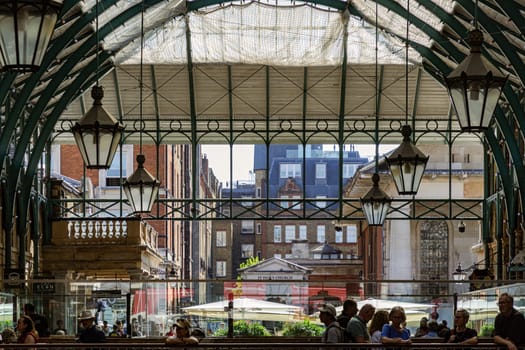 London, UK - May 13, 2025 - The vintage iron glass roof with Lamps on the ceiling of Apple market in Covent Garden Market Hall. View of Metallic framework arch roof with ceiling hanging lamp, use it as your Wallpaper, Poster and Copy space, Selective focus.