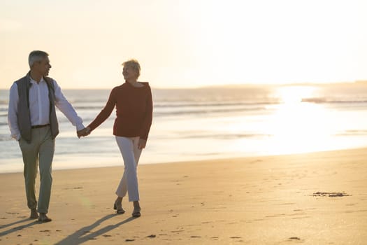 Senior couple holding hands and walking on the beach at sunset