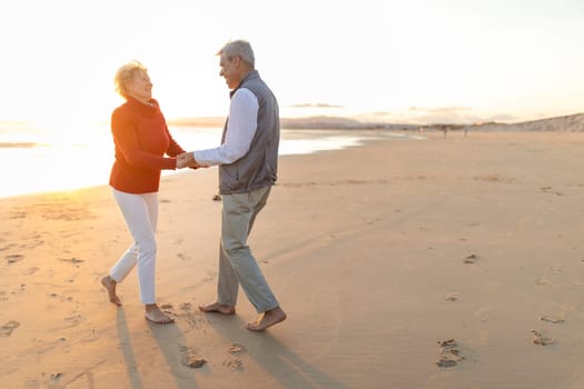 Elderly couple holding hands and dancing on the beach at sunset, enjoying retirement