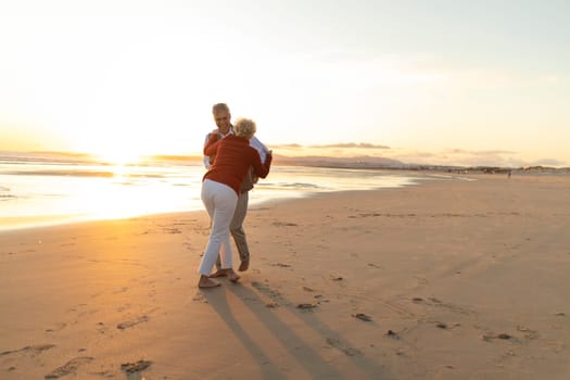 Happy retired couple dancing together on the beach at sunset
