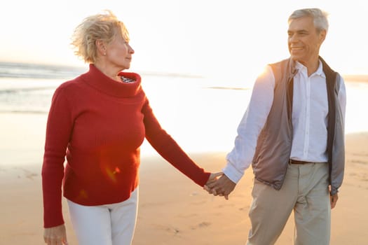 Senior couple enjoying a romantic walk on the beach at sunset, holding hands and smiling