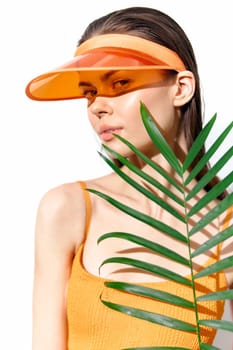 A vibrant summer portrait of a young model wearing a stylish orange visor and a matching top, holding a palm leaf, perfect for tropical fashion concepts.