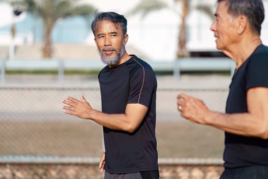 Two senior Asian men enjoy a lively jog, emphasizing their commitment to fitness and wellness in a friendly outdoor environment.