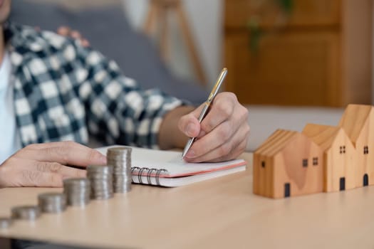 A focused LGBTQ couple strategizing their financial future by writing in a notebook, surrounded by coins and wooden houses, showcasing their commitment to shared goals in a cozy home environment.
