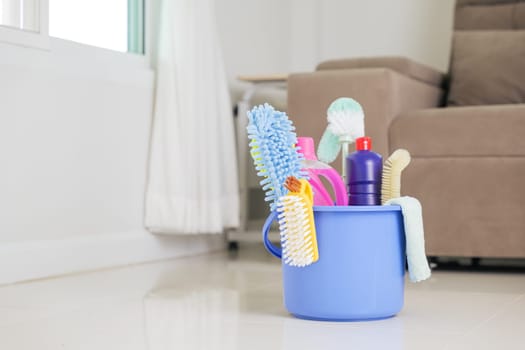 Cleaning essentials at home. A blue bucket containing detergent bottles, brushes, and other supplies sits on the floor in the living room, helping with routine housework and general housekeeping.