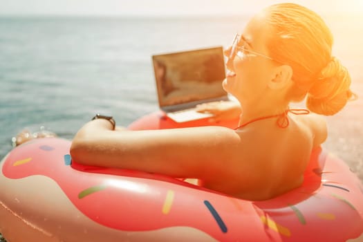 Woman laptop sea. Freelancer woman in sunglases floating on an inflatable big pink donut with a laptop in the sea. People summer vacation rest lifestyle concept
