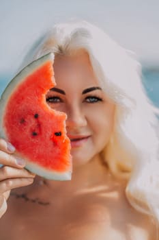 Blond woman with a bite taken out of a watermelon slice held to her face, partially obscuring her features. Beach background visible.