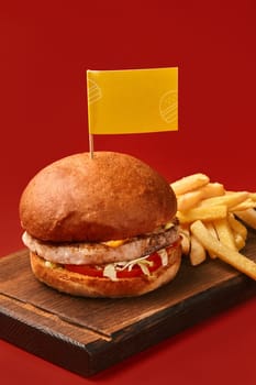 Tasty burger with meat, cheese, salad, tomato and french fries on wooden board is waiting to be eaten