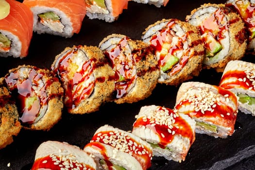 Delicious assortment of uramaki, tempura maki and hosomaki sushi rolls with salmon, avocado and eel, beautifully arranged on a black stone plate