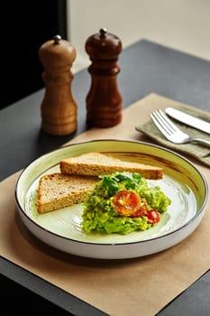 Healthy guacamole with toasted bread, cherry tomatoes and coriander served on a plate in a restaurant