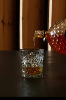 Golden liquid pouring from a bottle into a crystal glass on a dark bar top