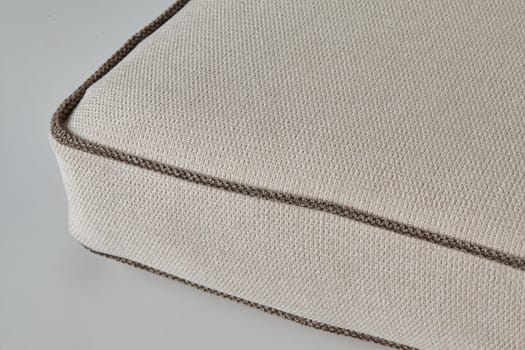 Close-up of beige fabric cushion with brown border detail, showing weaving and texture