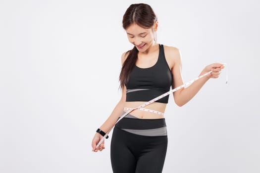 Measure inches lost and measure the joy she feels, this slim woman in fitness wear uses a tape to track her success, celebrating health and confidence. isolated studio white background