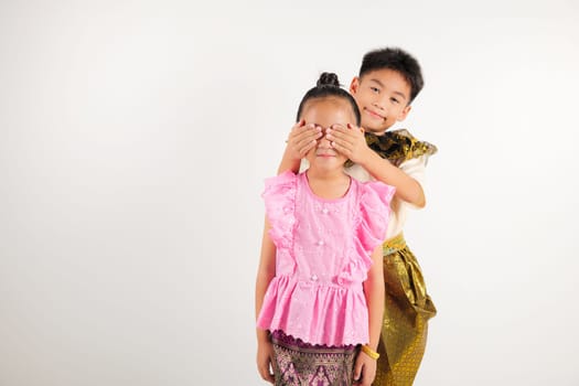 Portrait Thailand kid girl and boy traditional Thai dress costume together close eyes with hands play guess who or hide and seek studio isolated white background, Happy children hiding behind his back