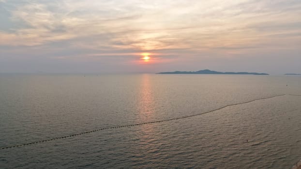 Golden hues of sunset paint the sky over a tranquil ocean, its surface reflecting the light as distant islands silhouette against the horizon, creating a serene and picturesque seascape
