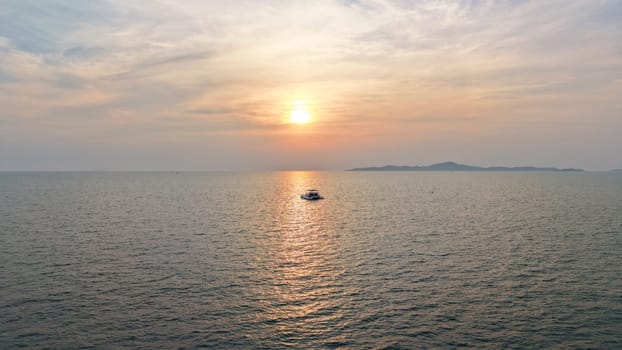 Golden sun setting over a tranquil ocean, casting a warm glow on the water as a catamaran sails peacefully towards the horizon, with a distant island adding to the serene seascape
