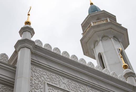 View from below the beautiful white stone minaret of the mosque with geometric patterns on the walls and crescent moon rising against the sky