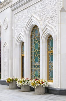 The white stone wall of the mosque with traditional Arabic floral ornamentation and large stained glass windows.