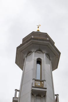 View from below of the mosque's beautiful white stone minaret with geometric patterns on the walls and a crescent moon rising against the sky, vertical
