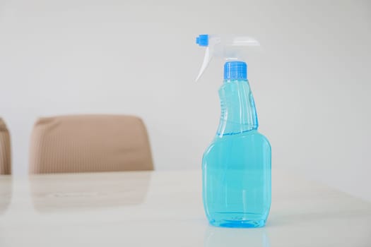 Blue glass spray bottle with white trigger in the kitchen table on a white wall background. The bottle is filled with clear blue liquid, Cleaning concept