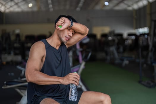A man in a gym wiping sweat and drinking water, emphasizing hydration and fitness recovery.